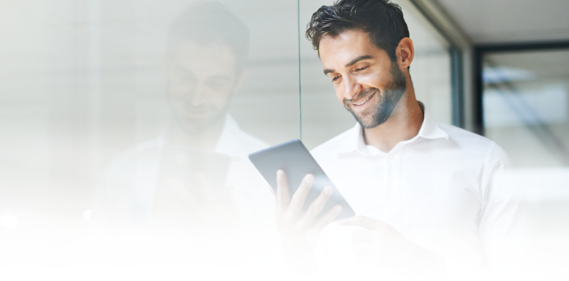 A man in an office smiles as he looks at a tablet.