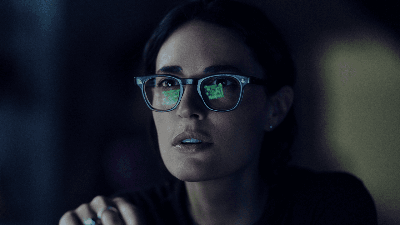 Close-up of a woman with parted lips looking up with a startled expression, green data reflected in her glasses lenses, lit dimly against a dark background.